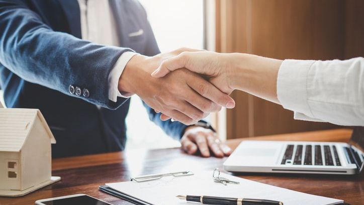 A real estate agent and client shaking hands together celebrating a finished contract.