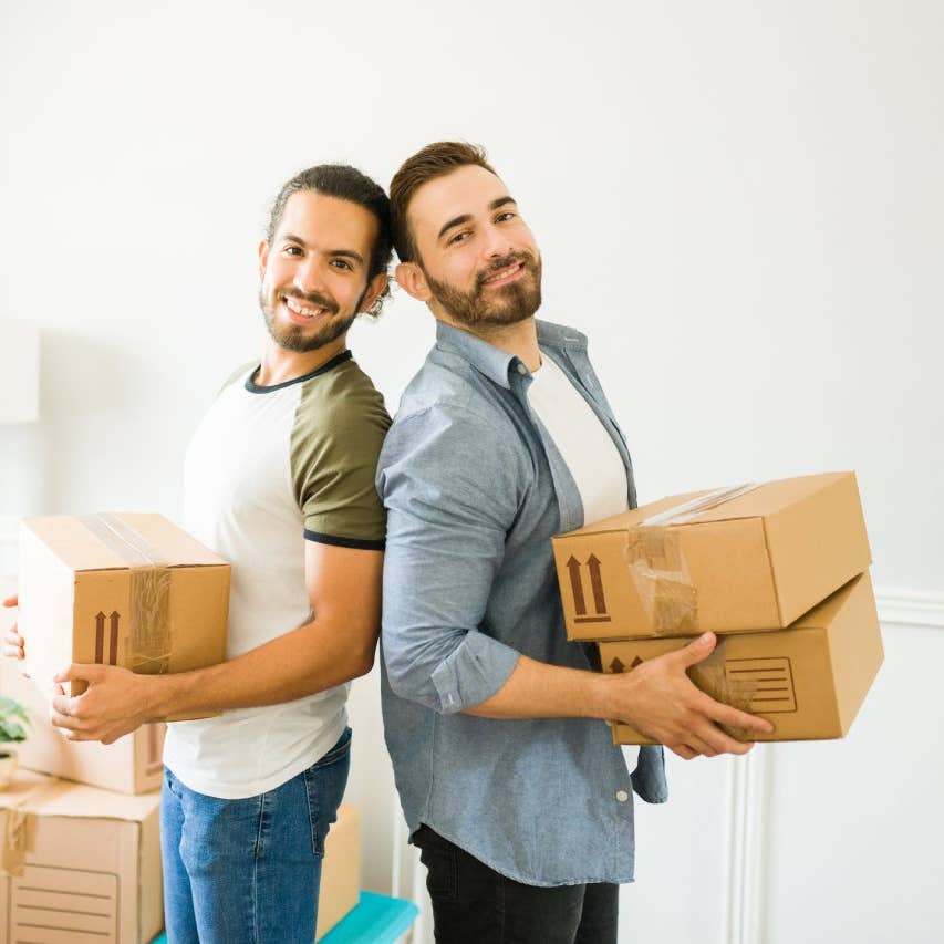 Smiling attractive man and his gay partner looking happy while carrying boxes to move in together