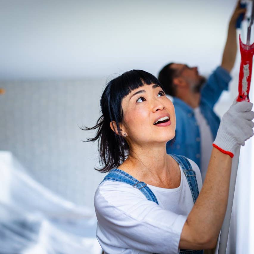 Happy couple renovating their home, painting the wall and smiling while working together
